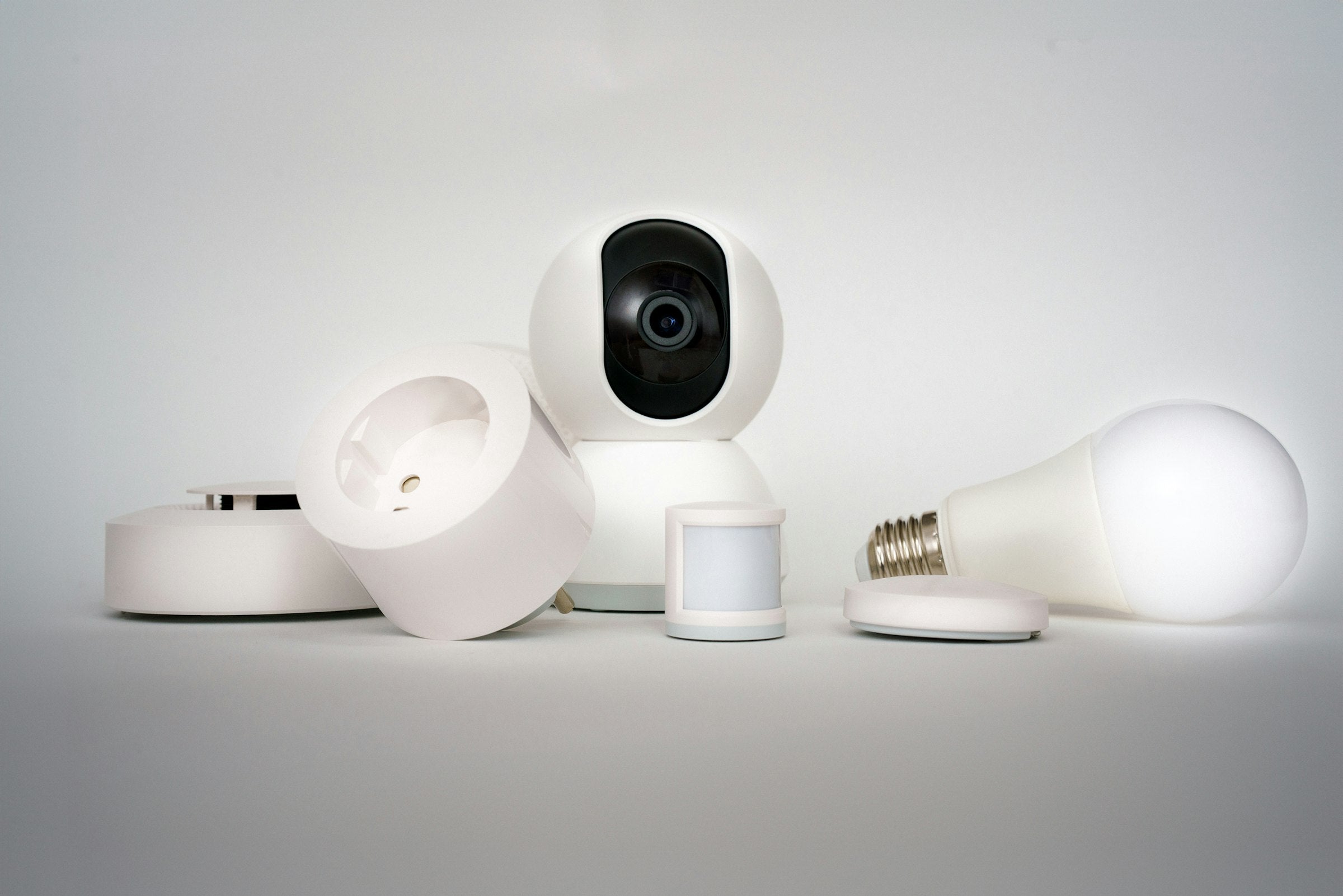 Collection of white smart home gadgets including a camera, smart plug, motion sensor, and smart bulb
